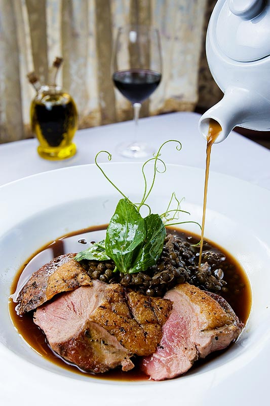 Ripasso duck jus poured over Anatra Alla Lenticchia, a seared duck breast with lentils, pancetta, duck confit and pea vines at La Dolce Vita in Seattle. (Photographer: Andy Rogers)